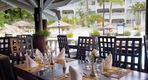 A restaurant setting with tables set for dining, outdoor umbrellas, and a view of a building with balconies. - Beautiful Luxury Villa in VIP All Inclusive Resort (Puerto Plata)