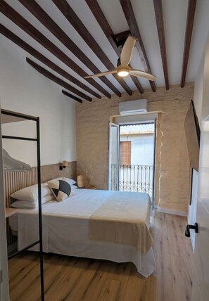 A bedroom with a bed, a ceiling fan, a window, and wooden beams. - Renovated Apartment with Air Conditioning - Just Steps from the Beach (Alicante (Alacant))