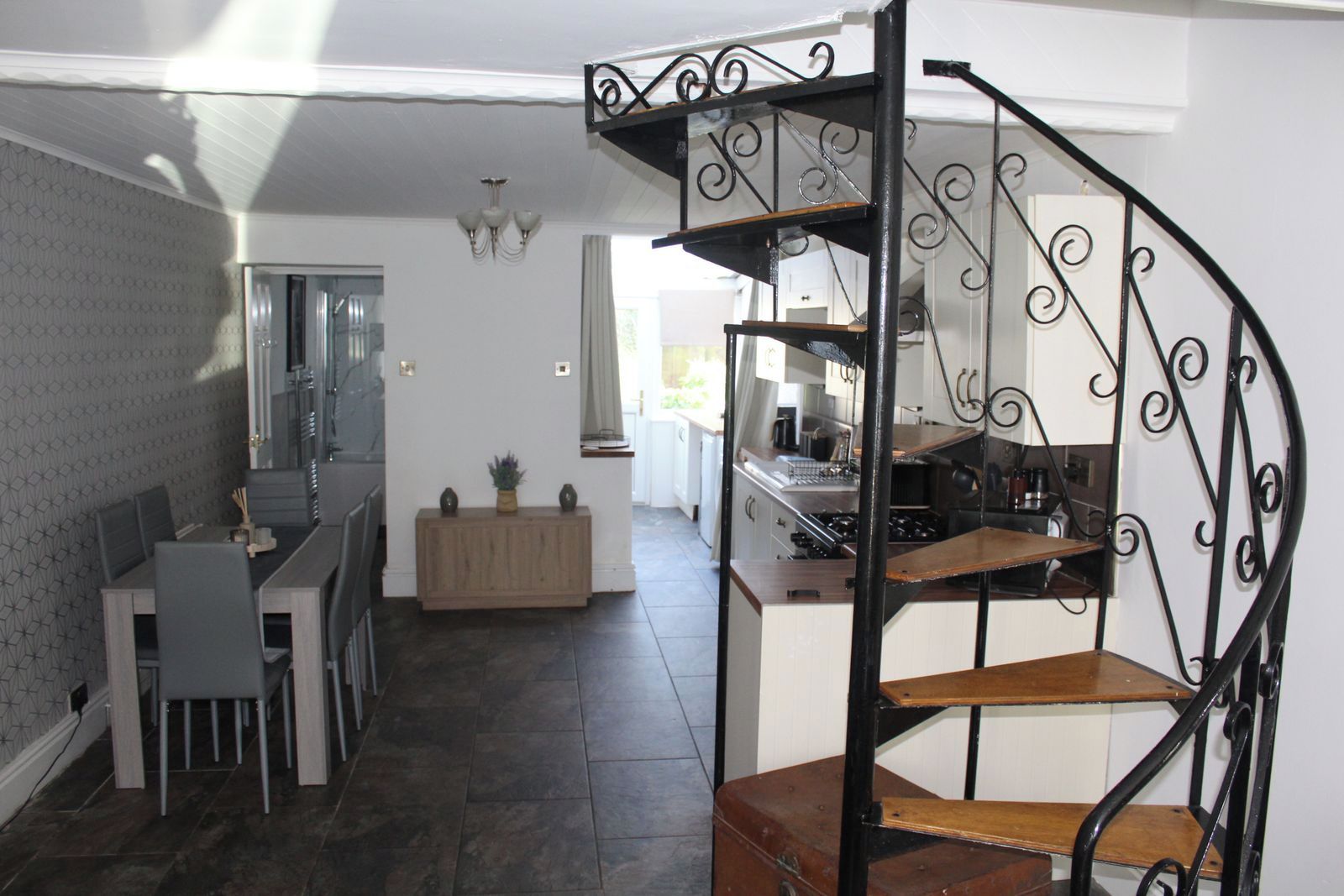 A modern kitchen with a spiral staircase, a dining area with a table and chairs, and a view into the living area.