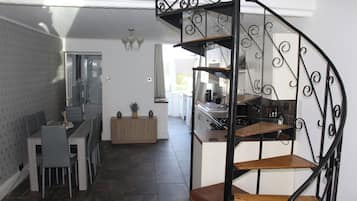 A modern kitchen with a spiral staircase, a dining area with a table and chairs, and a view into the living area.