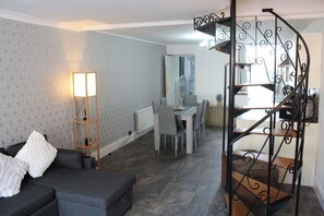Una sala moderna con un sofá gris, una lámpara de pie y un comedor con mesa y sillas.