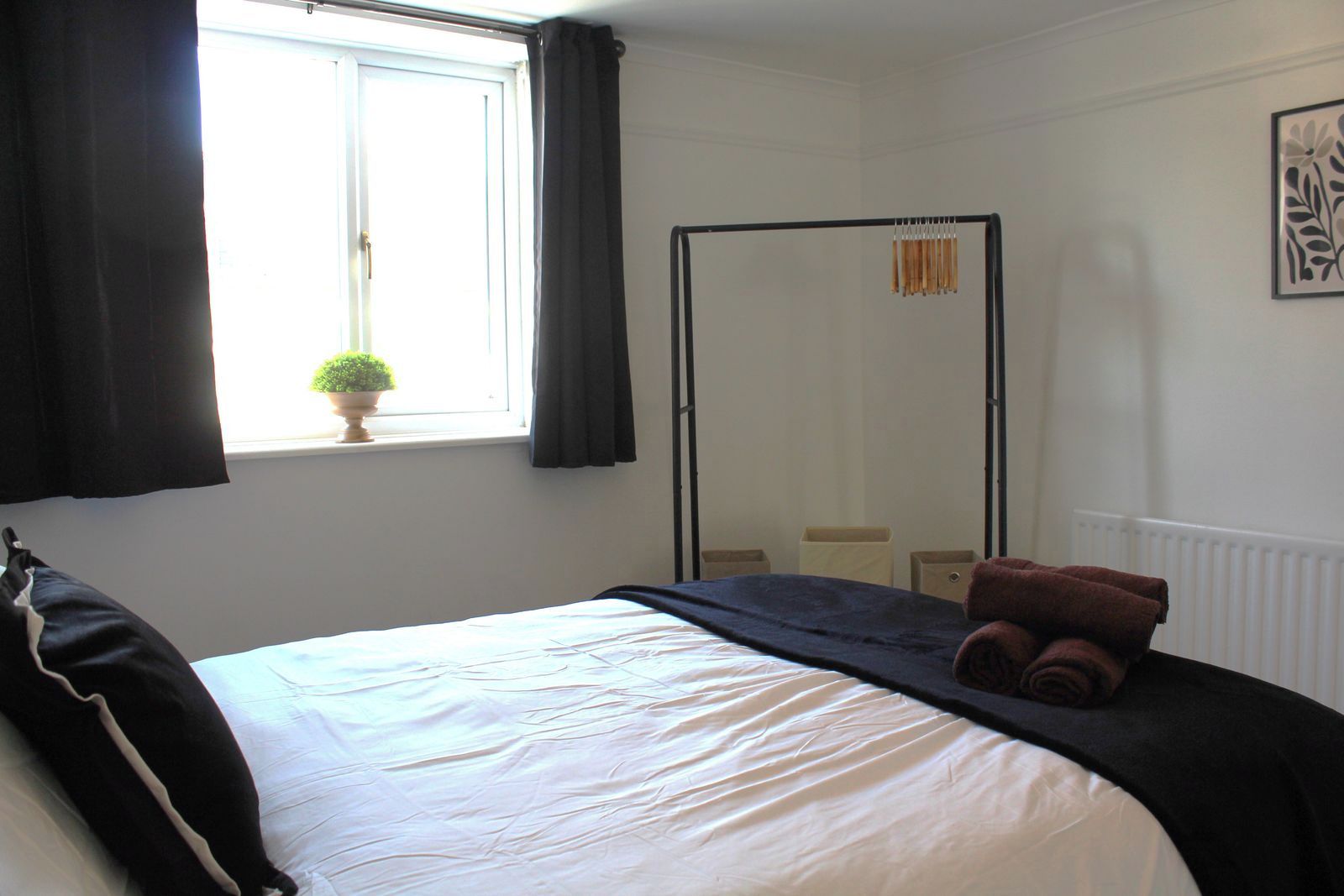 A hotel room with a bed, a window with curtains, a potted plant, a towel, and a mirror.