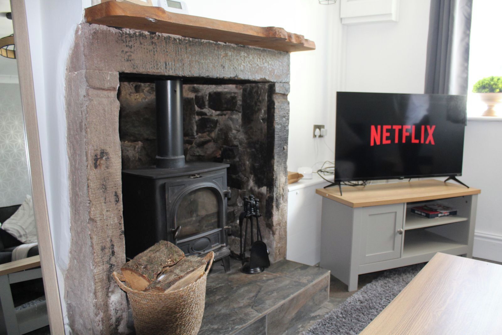 A living room with a stone fireplace, a television on a stand, and a basket of firewood.