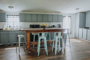 A kitchen with a central island, bar stools, and light blue cabinets. - Lowcountry Retreat (Olar)