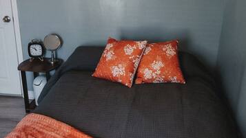Un letto con una coperta grigio scuro, due cuscini arancioni decorati con motivi floreali bianchi e una coperta coordinata arancione.