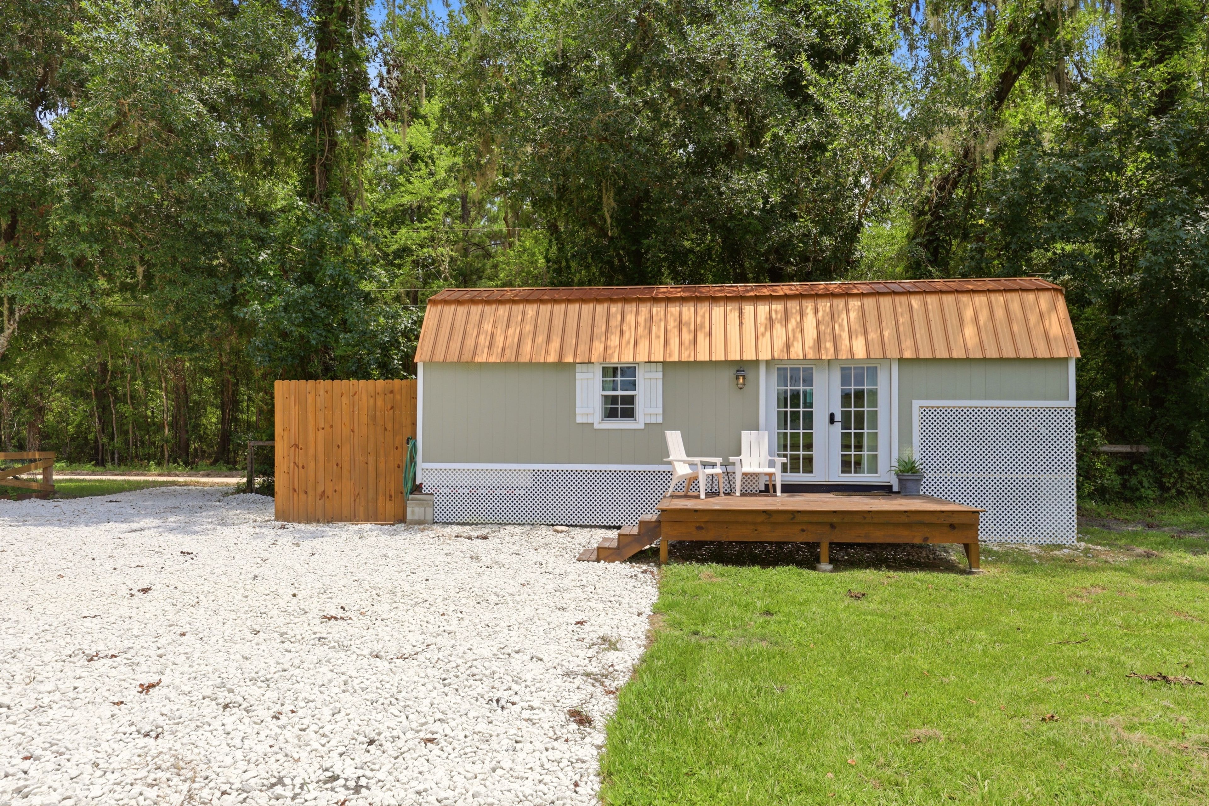 Una pequeña cabaña de madera con camino de grava y un área verde frente a ella.