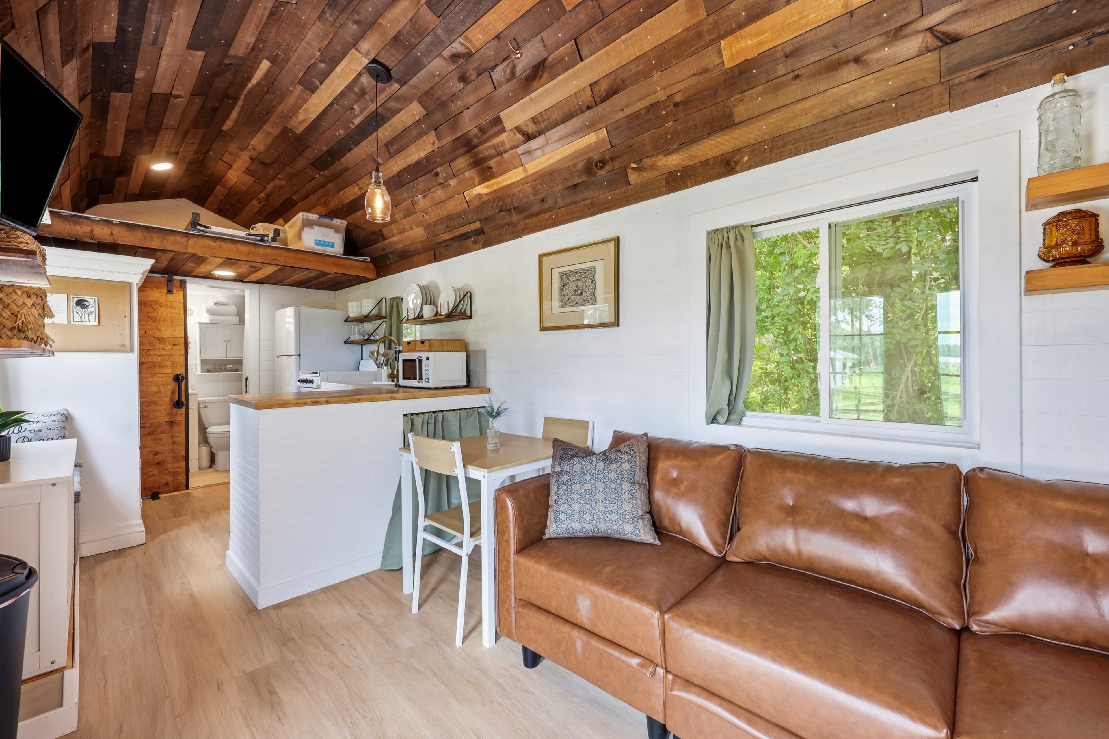 A cozy interior with a wooden ceiling, a kitchenette, a dining area, and a leather sofa.