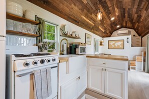 A kitchen with white cabinets, a stove, a microwave, and a hanging light fixture.