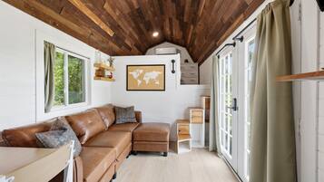 Een knus interieur met een houten plafond, een bruine leren bank, een wereldkaart aan de muur en een schuifdeur van glas.