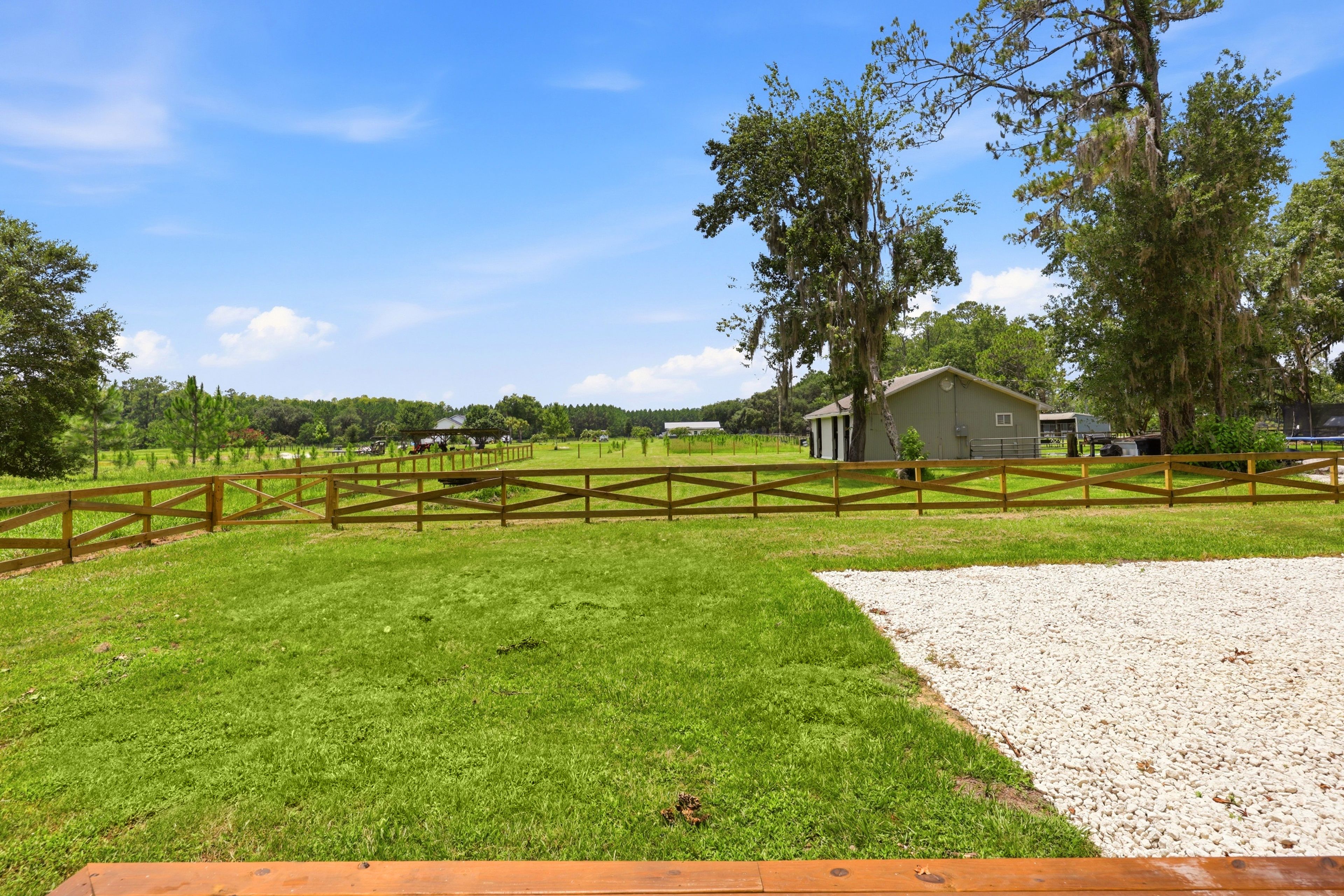 A fenced outdoor area with a gravel path, a grassy field, and a building in the background.