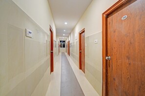 A hotel corridor with doors on both sides, a tiled floor, and a ceiling with recessed lighting. - Classic Gachibowli Bus Terminal (Hyderabad)