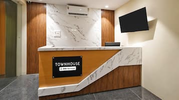 A reception desk with a marble top, a sign indicating it is serviced by OYO, and a flat-screen TV mounted on the wall.