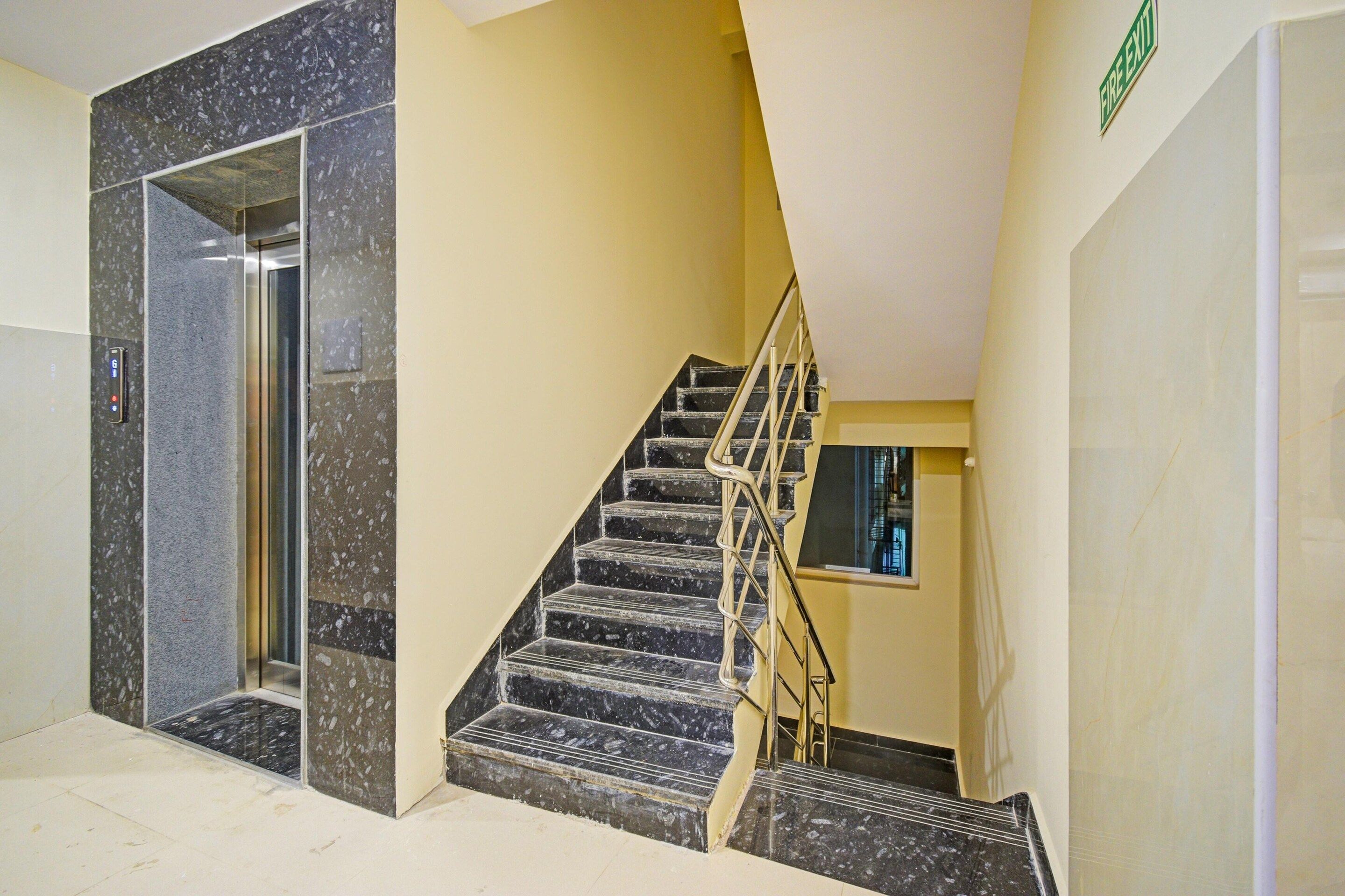 A staircase with a handrail, a fire exit sign, and a glass elevator door.