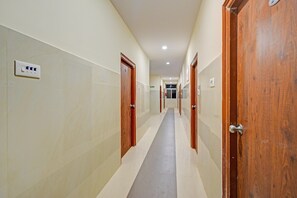 A corridor with wooden doors, a light switch, and a fire exit sign. - Classic Gachibowli Bus Terminal (Hyderabad)