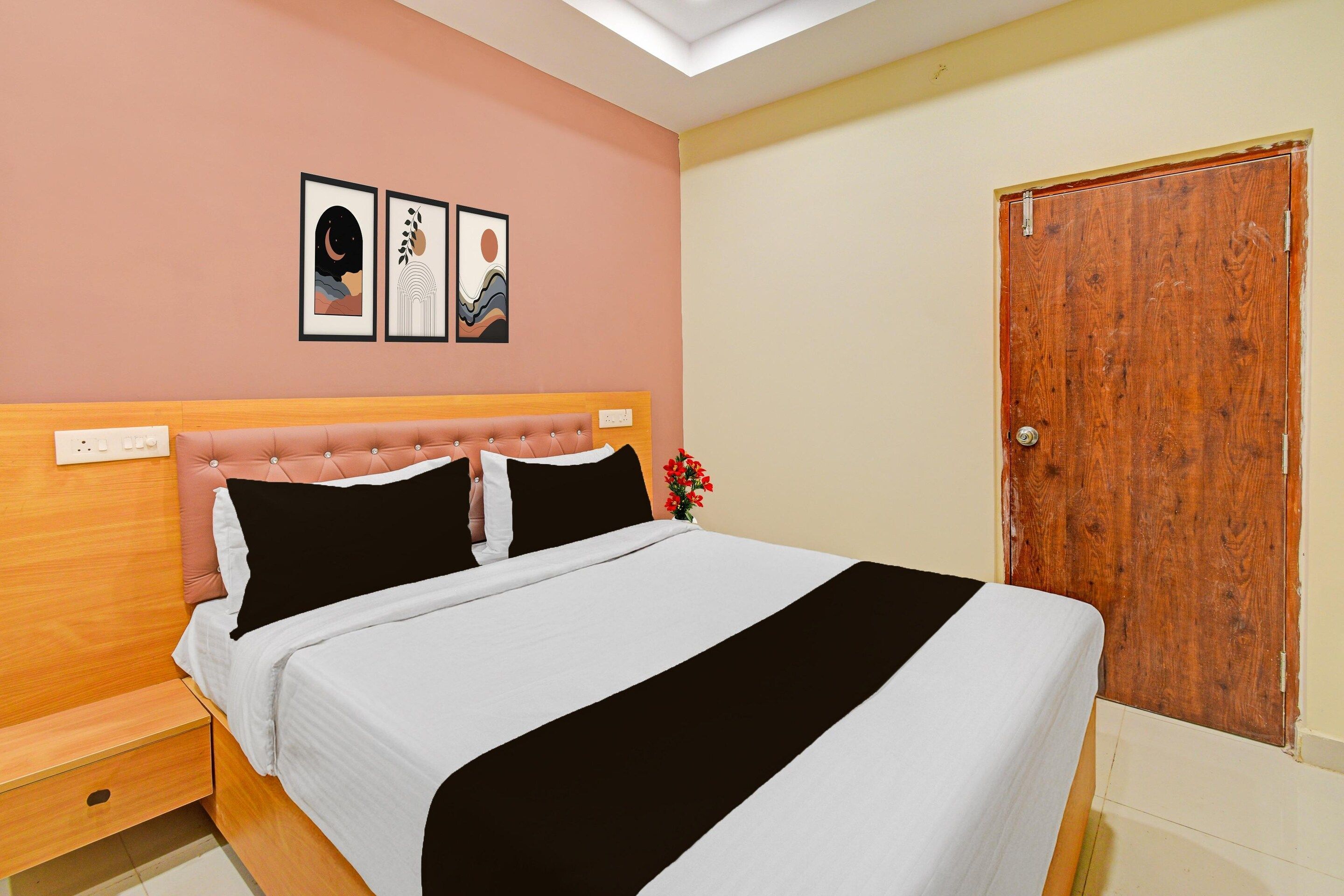 A bedroom with a bed, a nightstand, a wooden door, and two wall-mounted pictures.