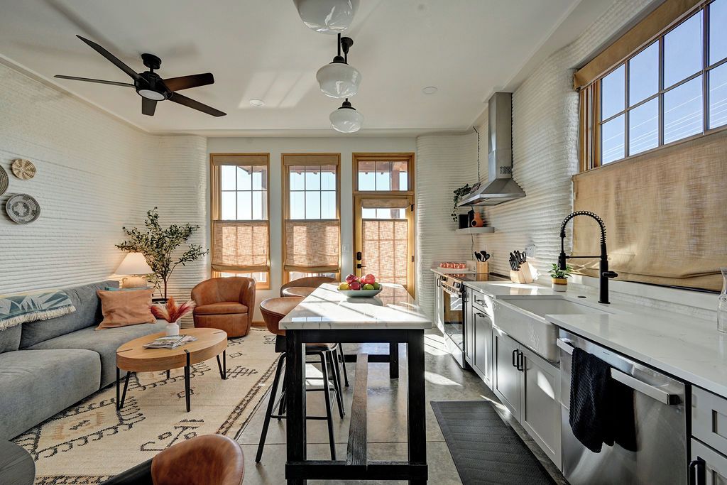 A modern kitchen with a central island, a dining area with a sofa and chairs, and a ceiling fan.