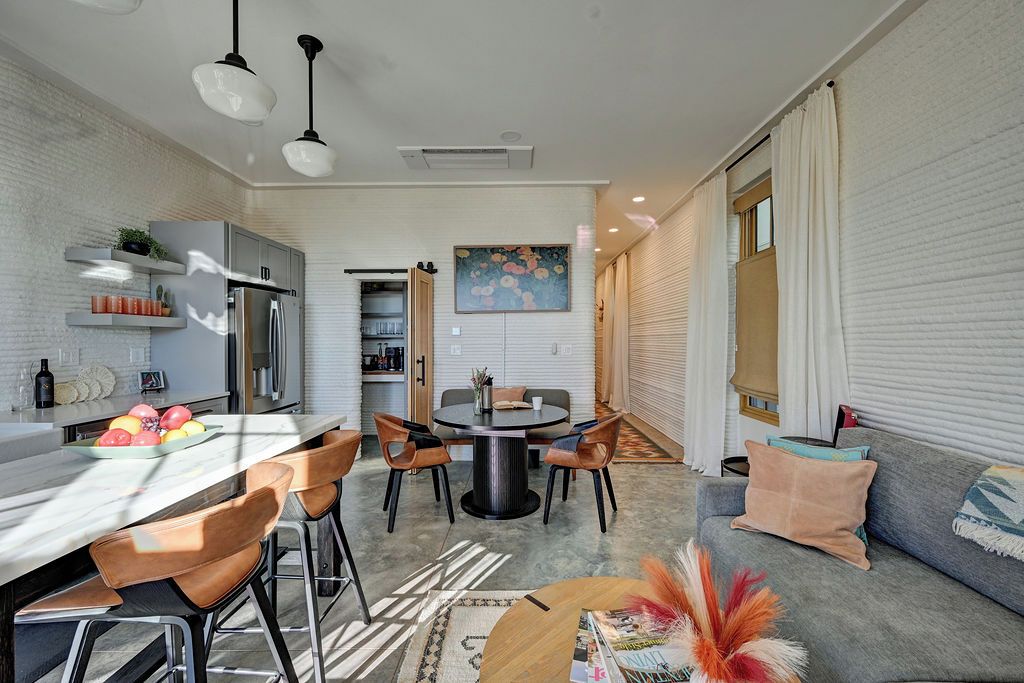 A modern kitchen with a dining area, a sofa, and a window with blinds.