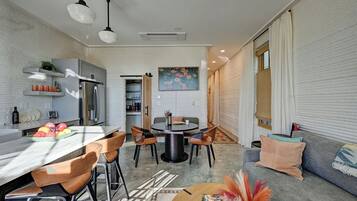 A modern kitchen with a dining area, a sofa, and a window with blinds.