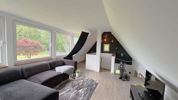 A modern loft bedroom with a large window, a built-in desk, and a seating area with a sofa.