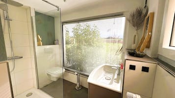 Ein modernes Badezimmer mit Glasdusche, Toilette, Waschbecken und einem Fenster mit Jalousien.