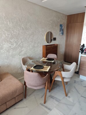 A dining area with a glass table, cushioned chairs, and a wooden cabinet.