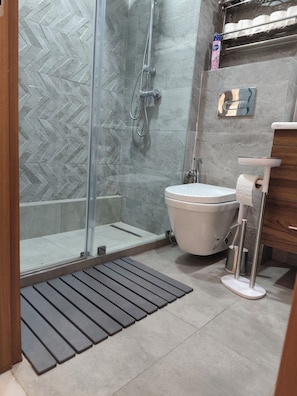 Een moderne badkamer met een douchecabine van glas, een toilet en een wastafel met een papieren handdoekdispenser.