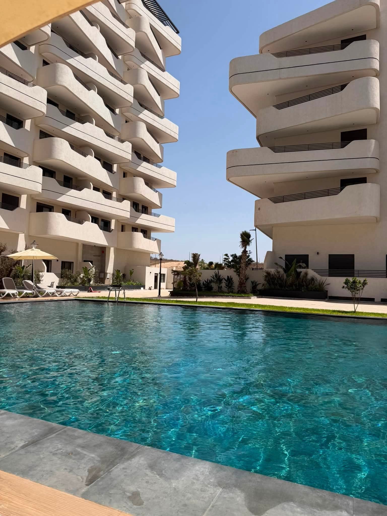 A modern hotel with a pool, multiple balconies, and a clear sky.