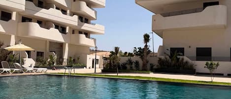 A modern hotel with a pool, multiple balconies, and a clear sky.