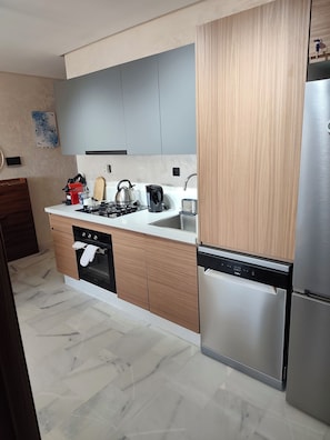 A modern kitchen with a gas stove, kettle, and dishwasher.