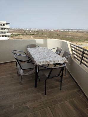 A balcony with a table and chairs, a view of a distant cityscape, and a building in the background.