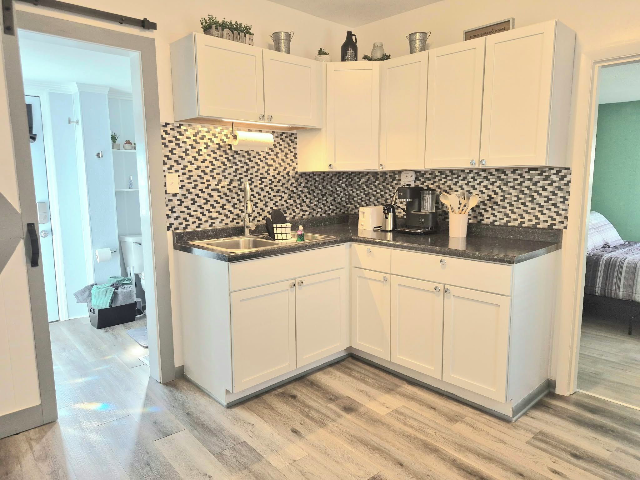 A modern kitchen with white cabinets, a black and white backsplash, and a coffee maker.