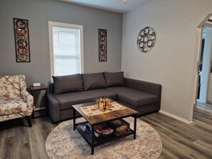 A living room with a gray sofa, floral armchair, and a coffee table with board games.