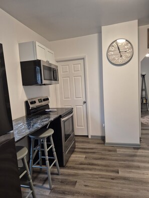 A kitchen with a black countertop, stainless steel appliances, and a wooden floor.