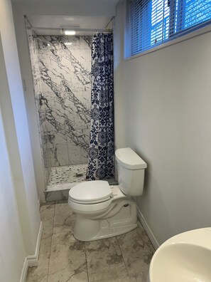 A bathroom with a toilet, shower, and a patterned curtain. - Central Oakville/Kerr Village:steps to shops, eateries, cinema, transit, & GO  (Oakville)
