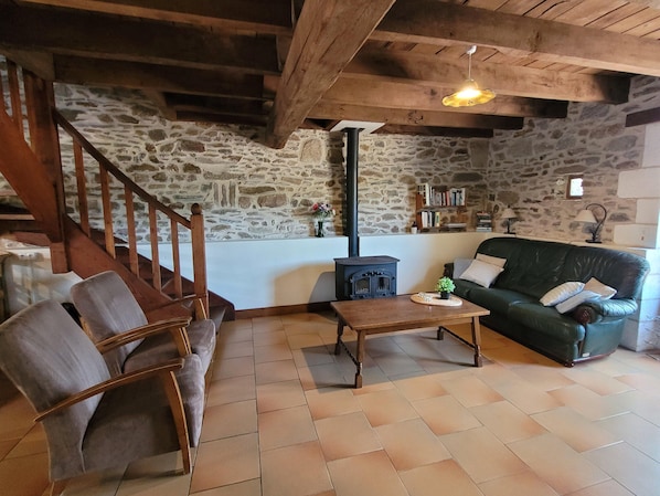 A cozy living room with a stone wall, a wooden staircase, a green sofa, and a wooden coffee table. - Authentic, Spacious Gite for 10 (Saint-Saud-Lacoussiere)