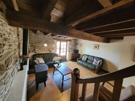 Un interior rústico con paredes de piedra, techo de madera, sofá de cuero verde, una mesa de madera y una escalera.