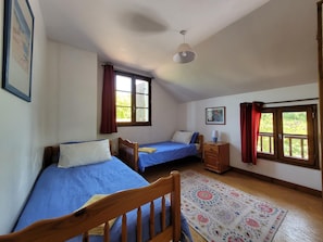 A bedroom with two single beds, a wooden nightstand, a ceiling fan, and a window with curtains. - Authentic, Spacious Gite for 10 (Saint-Saud-Lacoussiere)
