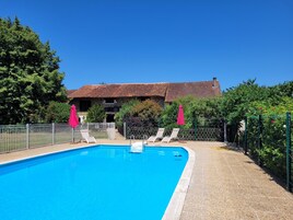 Una piscina con sillas de descanso y sombrillas, rodeada por una cerca y árboles.