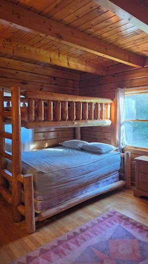 A wooden cabin room with a bed, a window, and a wooden headboard. - Cozy 3 bedroom with loft cabin in serene Pittsburg with AC & woodstove. (Pittsburg)