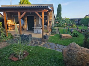 A covered outdoor seating area with a brick wall, a wooden pergola, and a stone pathway leading to a door. - Cozy little bungalow with a fireplace and pool in a quiet location—5 minutes from the F60 (Heideland)
