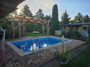 A backyard with a swimming pool, a wooden pergola, and a hanging swing. - Cozy little bungalow with a fireplace and pool in a quiet location—5 minutes from the F60 (Heideland)