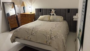 Een slaapkamer met een bed, een kaptafel, een spiegel, een lamp en een knuffel.