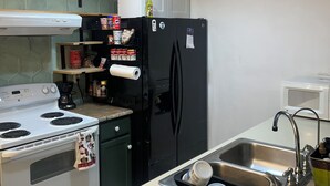 Een keuken met een witte kookplaat, een zwarte koelkast en een roestvrijstalen spoelbak.