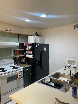 Cocina con estufa blanca, refrigerador negro y pileta de acero inoxidable.