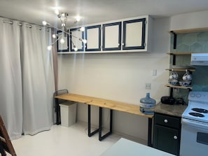 Una cocina compacta con estufa integrada, dispensador de agua y una mesa de madera.