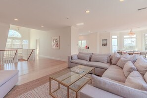 A spacious living room with a large sectional sofa, a glass coffee table, and a staircase leading to another level. - Cape Mayzing! Pool, Sleeps 12, West Cape May (West Cape May)