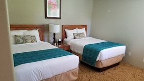 Dos camas individuales con cabeceras y pies de cama a juego, una mesita de noche con lámpara y una alfombra estampada.