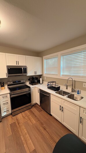 A modern kitchen with white cabinets, stainless steel appliances, a dishwasher, and a sink.