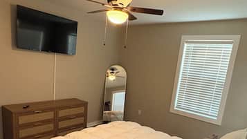 Een slaapkamer met een bed, een plafondventilator, een televisie, een dressoir en een raam met jaloezieën.