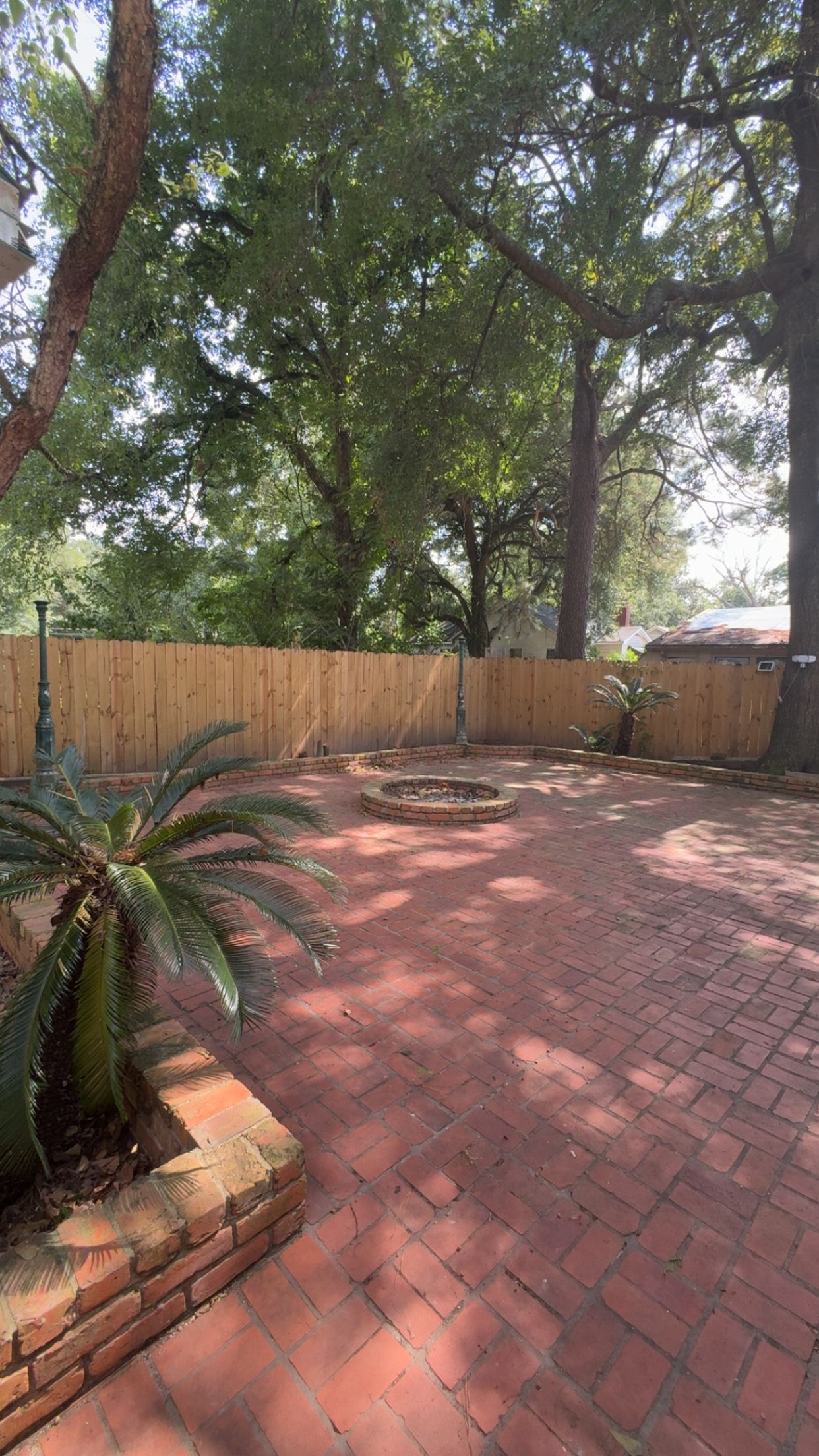 Un patio de ladrillo con valla de madera y árboles.